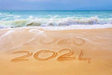 2024 written on the sand of a beach, ocean waves, travel new year greeting card