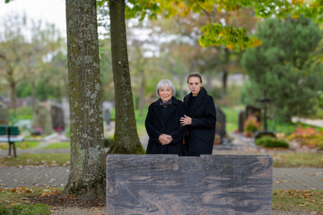 Mother and daughter standing at the man's grave and looking to camera