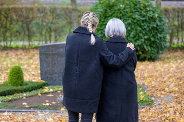 Fototapeta premium Daughter hugging her mother at the man's grave in the cemetery