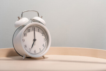 Close-up of a round white alarm clock on a table in the bedroom. The hands on the clock show seven...