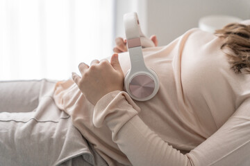 Pregnant asian woman holding headphone on belly playing music to her baby in stomach relaxing...