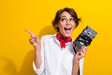 Photo of astonished cute person hold movie videocassette look direct finger empty space isolated on yellow color background - obrazy, fototapety, plakaty