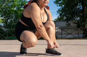 Young black girl with african braids puts on her running shoes in a park outdoors. Latina plus size...