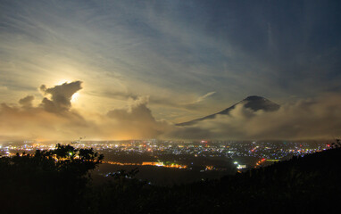 Naklejka na ściany i meble Giant cloud wave approaching Mt. Fuji and city lights on full moon night