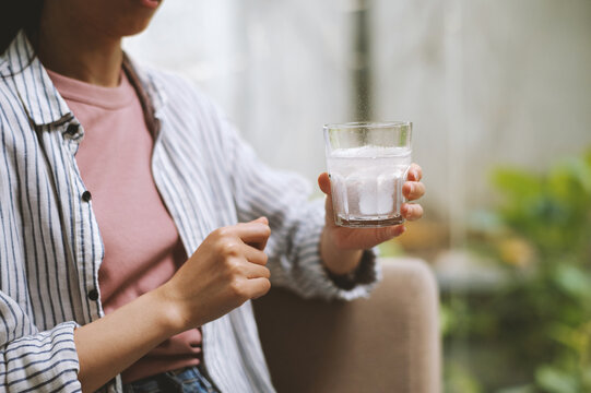 Cropped image of young woman taking glass of water with fizzy tablet