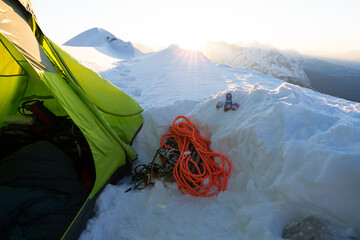 Winterbiwak im Schnee auf einem Berg in den Alpen mit grünem Zelt zum Sonnenaufgang