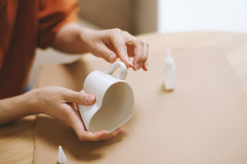 Closeup image of person repairing ceramic heart shape tea cup - obrazy, fototapety, plakaty