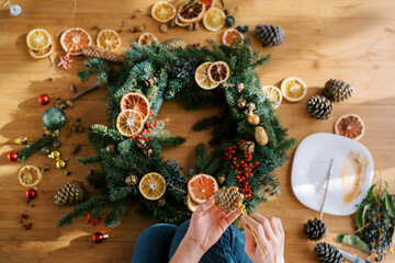 Artist applies paint to a pine cone with a brush near the Christmas wreath. Cropped. Top view