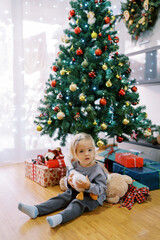 Obraz na płótnie Canvas Little girl with a toy duck sits on the floor near the Christmas tree