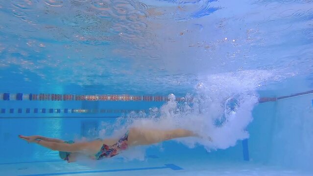 Woman athlete swims underwater in the pool. Slow motion of a female swimmer in the pool during training. The swimmer dives deep underwater.