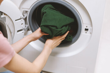 Young woman taking fresh clean clothes out of washing machine