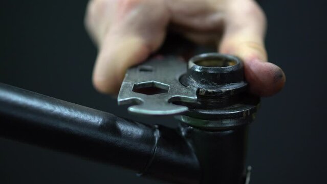 A mechanic in the workshop repairs an old frame of a classic bicycle. Replacing the grease and bearing in the headset, installing the fork in the frame, tightening the nut and the headset cone.