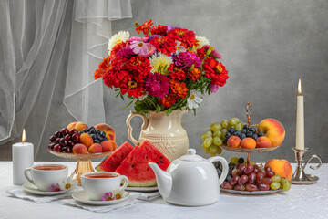 Breakfast and flowers and candles on the table. Cups, teapot and fruits in a vase