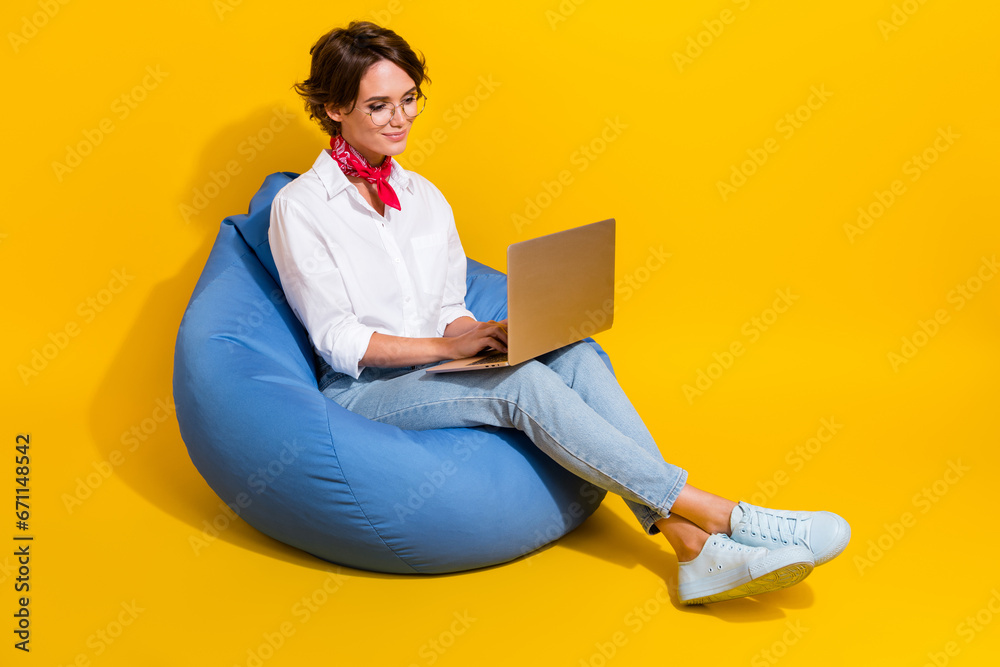 Poster Photo of adorable cute girl sitting soft pouf using modern device wireless netbook macbook empty space isolated on yellow color background