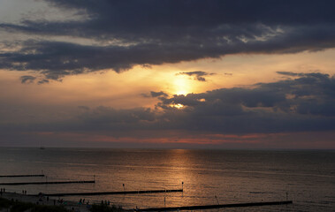 View of the setting sun over the calm sea under a cloudy sky.