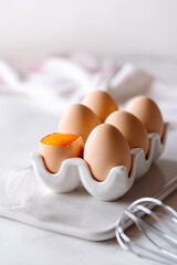 eggs on a glass stand on a light background, one egg is broken and the yolk is visible, soft light,...