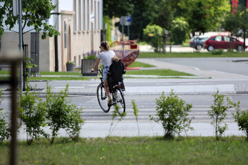 Kobieta z dzieckiem na bagażniku jedzie rowerem przez przejście dla pieszych - obrazy, fototapety, plakaty
