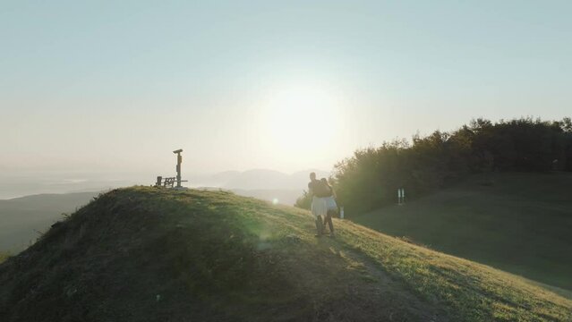 Fit couple walking and hiking to the top of the hill. Enjoying and exploring green countryside. Beautiful nature at sunset.