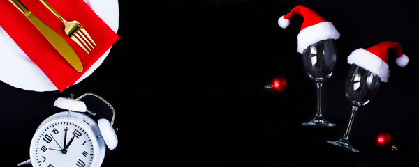Christmas table setting and wine glasses with Santa Claus hat on the black background. Copy...