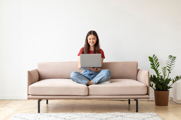 Beautiful Young Asian Woman Using Laptop While Sitting On Couch At Home
