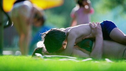 Candid loving moment between mother and child laid on grass during summer day activity, little boy...