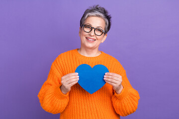 Photo of pretty sweet lady wear knitted pullover spectacles holding blue heart isolated purple color background