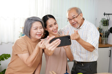 asian family senior couple with granddaughter talking selfie from smartphone, making miniheart sign and duck face at home