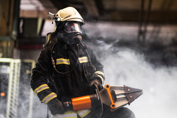 Fireman portrait wearing full equipment and oxygen mask. Firefighter with power hydraulic cutting...
