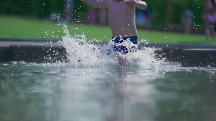 Happy child running in swimming pool water in slow-motion during summer day. Active little boy splashing water runs forward in 120fps
