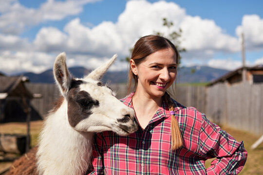 Young woman in shirt standing next to white llama at zoo on a sunny day, smiling, posing for picture