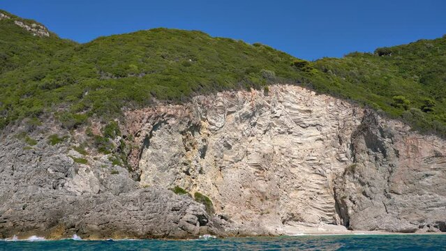 Sharp tall rocky cliffs visible above water, geological layers of rock - typical seascape near Liapades, Corfu Greece, view from a boat