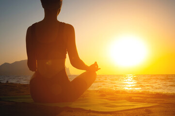 girl does yoga and meditates in lotus position on the beach. silhouette of a young woman by the sea...