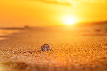 Fototapeta na wymiar compass on the beach with sunrise or during sunset, orange sky with bright sun rays, travel concept