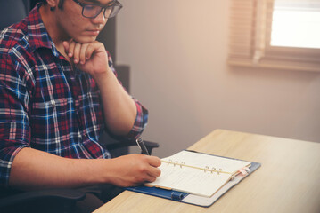 Male hand of planner writing diary, working space at home. Man plan and noted schedule (holiday trip), and daily appointment On Calendar book at office desk. Planner concept.