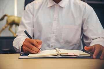 Male hand of planner writing diary, working space at home. Man plan and noted schedule (holiday trip), and daily appointment On Calendar book at office desk. Planner concept.