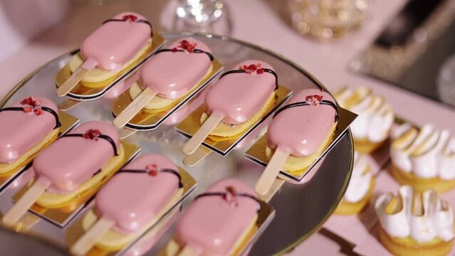 Festive candy bar. Close up of sweet buffet with yummy cakesicles in pink glaze, decorated sublimated strawberries on mirror plate. Tasty dessert, close-up, delicious. Celebration event catering.