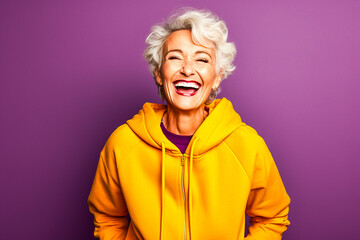 Femme sénior souriante avec un sweat jaune sur un fond violet - obrazy, fototapety, plakaty
