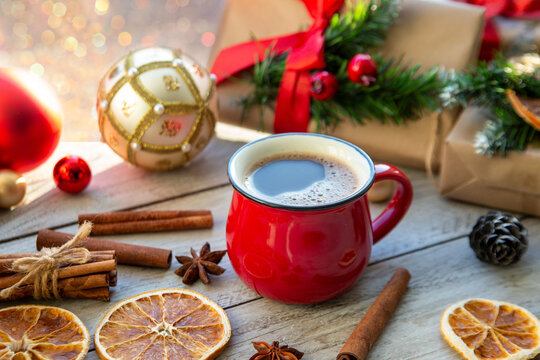Christmas mood, holiday atmosphere. Red cup of coffee, Christmas gift boxes, Christmas tree golden ball, cones, star anise, cinnamon on a wooden windowsill.