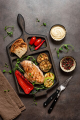 Fototapeta na wymiar Grilled chicken fillet with grilled vegetables, dark grunge background. Top view, flat lay, vertical. Healthy eating concept.