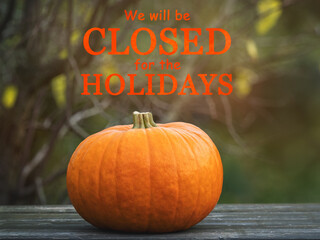 Signboard with the inscription We will be closed for the holidays. Bright, juicy pumpkin. Closeup, outdoors