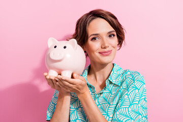 Portrait of pretty positive young girl arms hold money savings bank pig isolated on pink color...