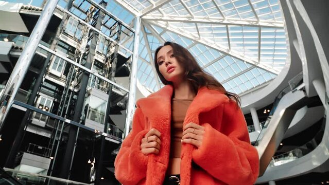 Portrait beauty female model in fashion orange fur coat posing at multilevel shopping center