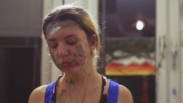 Portrait of a female artist. Girl with clumsy clorful painted face. Serious expression.
