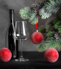 Christmas card. Fir branch with red balls, a bottle of wine and a glass on a black background