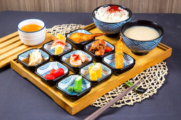 Assorted japanese food Mentaiko Chicken Wings, noodles soup, fried shrimp, sauce, ladyfinger vegetable and pork slice with chopsticks served on wooden board isolated on napkin side view on table