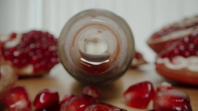 On a wooden table lies a bottle from which pomegranate juice is dripping. Pomegranate fruits and spilled juice. On a white background. Dolly slider extreme close-up.