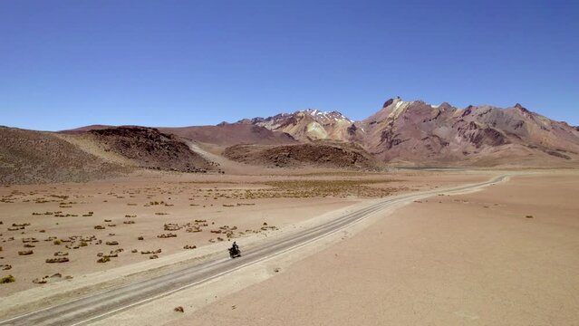 side vman on motorcycle followed by drone discovering a lonely desert road with mountains and lagoons 