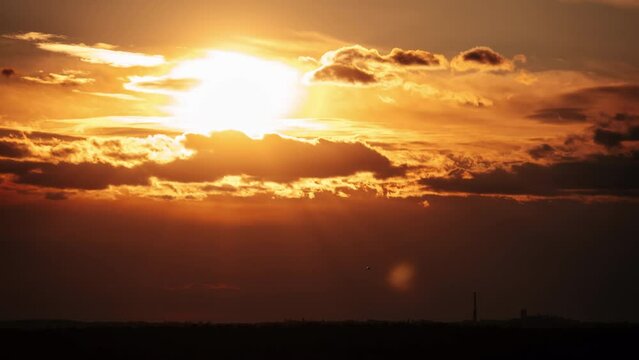 Timelapse awesome sunset moving down in orange sky with clouds. Bright orange sun moves down over the horizon behind the layered clouds. Epic cloud space, vibrant color. Time Lapse. Sundown 4K