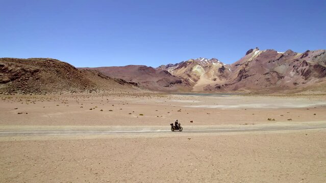 side vman on motorcycle followed by drone discovering a lonely desert road with mountains and lagoons 