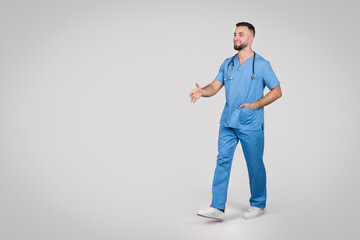 Young caucasian doctor man walking on grey background, full length, free space